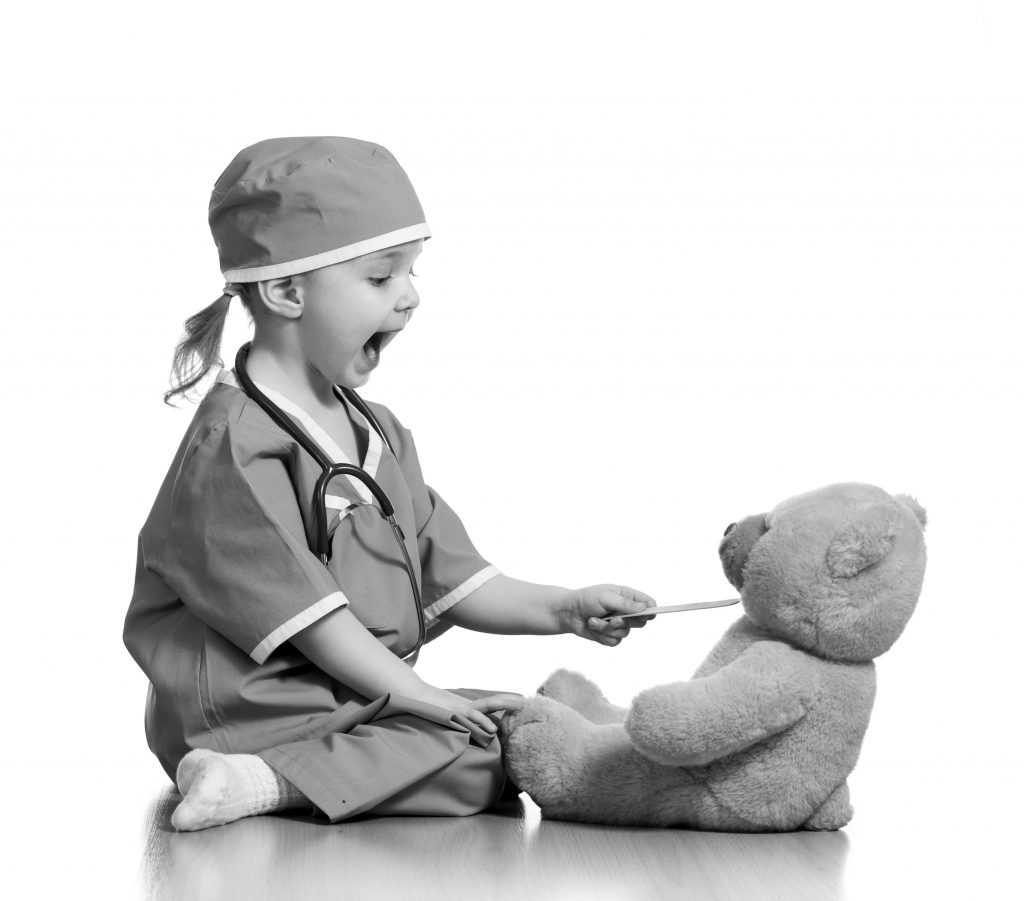 Adorable child dressed as doctor playing with toy over white background